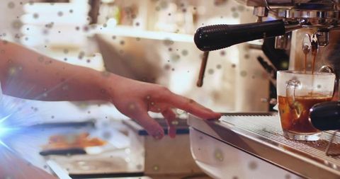 Barista steadying espresso shot glass on machine, crema pouring, cafe counter closeup