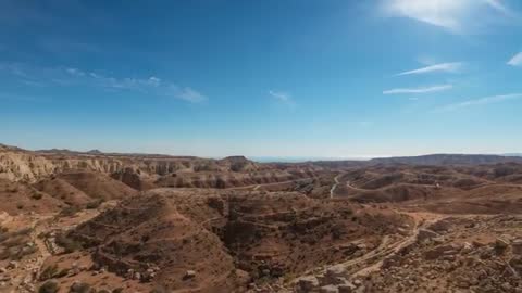 Drone Performing Slow Sweep Over Arid Canyon With Winding Dirt Tracks and Wide Plateau