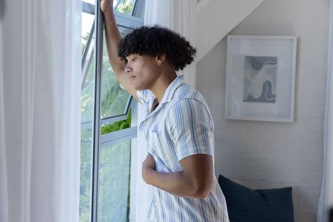 Young african american man leaning at window gazing outside, contemplating in bright loft
