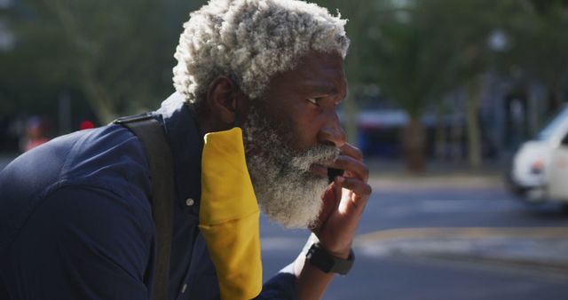 Elderly man with a beard speaking on a mobile phone while leaning on railing in an urban environment. Ideal for themes related to communication, modern technology use by seniors, urban life, and casual interactions.