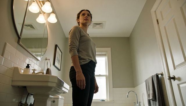 Woman standing in modern bathroom looking up near pedestal sink and mirror, soft daylight