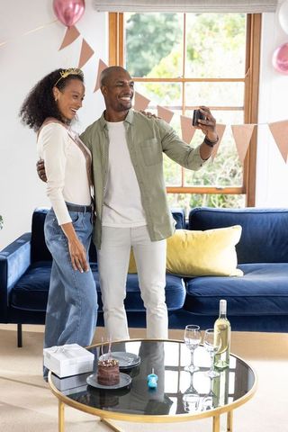 Couple taking selfie in decorated living room during intimate birthday celebration at home