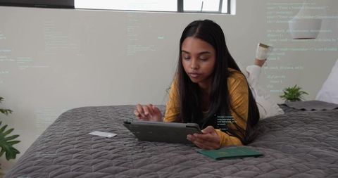 Woman in mustard top using tablet on bed with passport and programming overlay