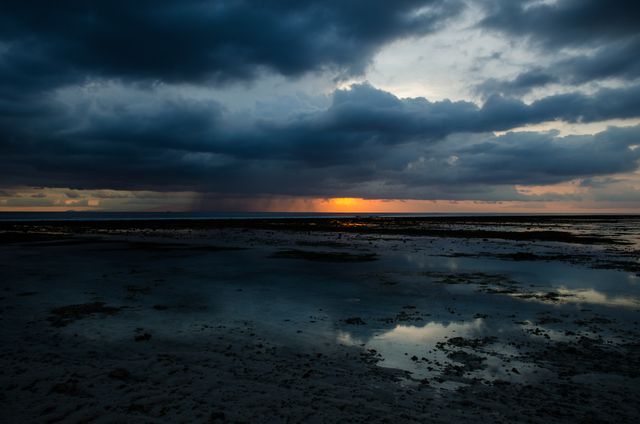 Sunset scene showing dramatic, stormy clouds over ocean with tide pools reflecting sky. Useful for projects related to nature, tranquility, coastal landscapes and environmental themes.