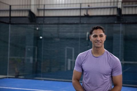 Athlete standing on indoor padel court wearing purple shirt and confident smile