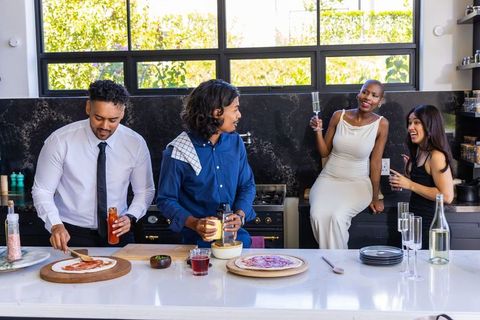 African american friends making pizza and toasting champagne in modern kitchen