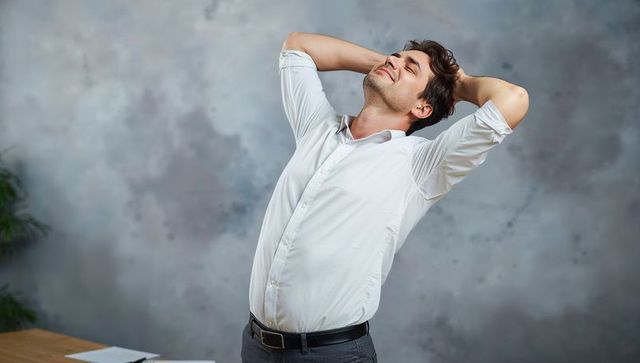 Young professional man stretching at desk, showing relief and workplace relaxation