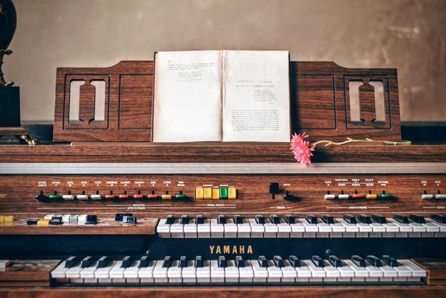 Perfect for retro-themed designs, music-related projects, or advertisements for music lessons. The image showcases a vintage Yamaha electric organ with a classic wood finish, an open music book, and a single flower, reflecting both nostalgia and a timeless appreciation of music.
