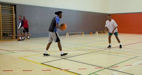 Young men playing pickup basketball in indoor gymnasium, dribbling, guarding, practicing