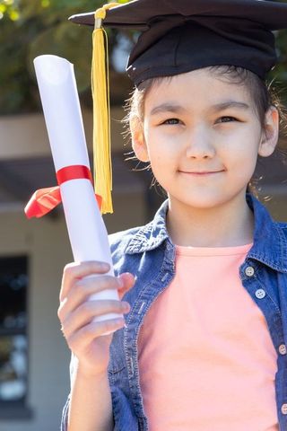 Asian girl celebrating graduation holding diploma wearing mortarboard and tassel outdoors