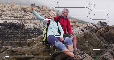 Middle-aged couple hiking on rugged coastal rocks taking selfie with data overlays