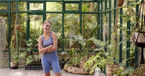 Confident Woman in Yoga Attire Posing in Elegant Greenhouse