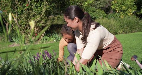 Parent child gardening teaching kneeling beside purple flowers sunlit backyard watering can