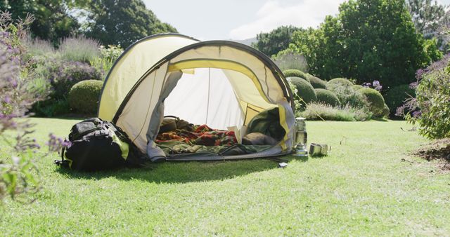 Yellow tent with blankets and pillows over trees in sunny garden. Nature, camping and lifestyle concept.