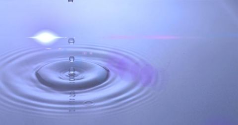 Water Droplet Creating Ripples on Calm Surface with Lens Flare
