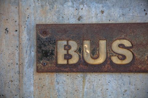 Weathered Metal Sign Spelling BUS on Concrete Wall