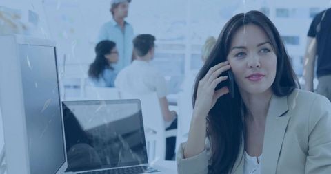 Professional woman talking on smartphone in bright open-plan office with laptop