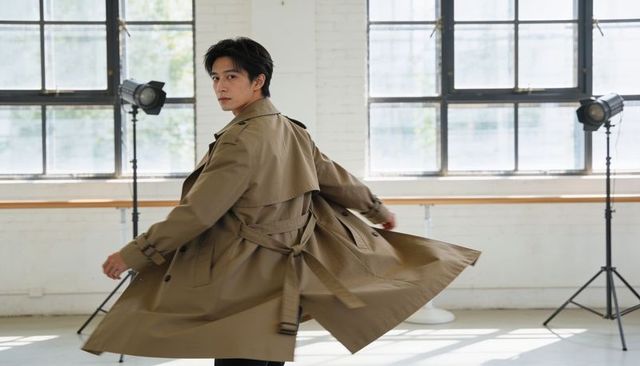 Spinning asian male model wearing khaki trench coat and dark trousers in studio lights