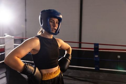 Female boxer standing in ring wearing blue headguard and gloves, focused and preparing