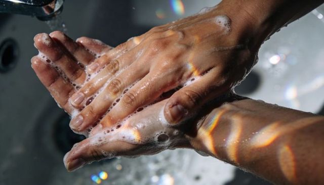 Closeup foamy hand washing with soap lather and iridescent light reflections at sink