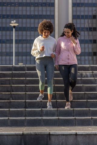 Two women walking down urban steps in activewear and sneakers for morning workout