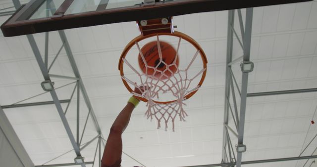 Basketball player performing a slam dunk, capturing the motion and athleticism in an indoor sports court. Ideal for use in sports magazines, fitness blogs, athletic campaigns, and advertisements promoting sports equipment or events.