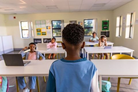 African american boy presenting to classmates in modern classroom with laptop