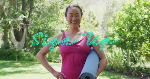 Korean woman holding yoga mat in sunlit backyard, smiling with neon sign up overlay