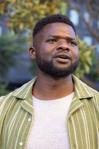 African man speaking and looking up outdoors wearing green striped shirt and gray tee