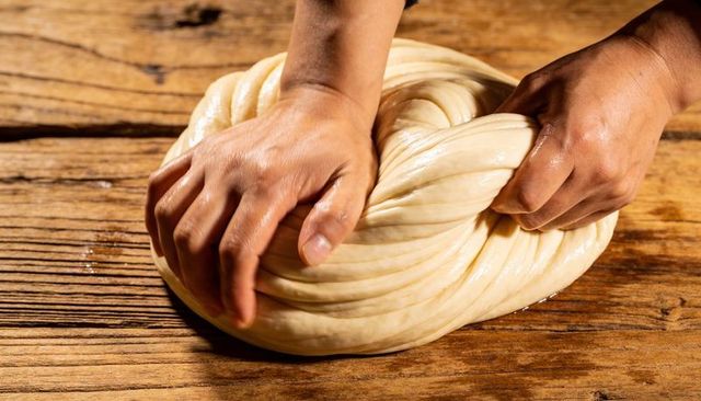 Kneading and braiding soft dough by hand on rustic wooden surface for artisan bread