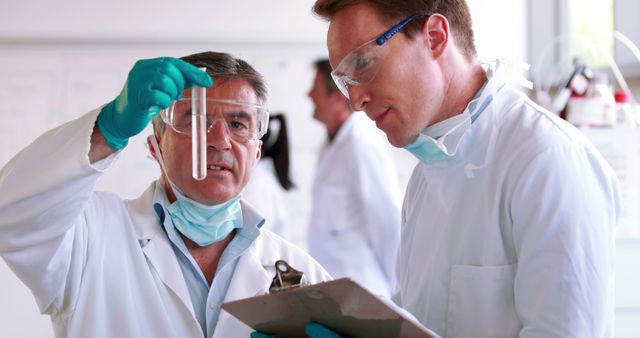 Scientists in white lab coats and safety goggles examining test tube in laboratory setting. Ideal for use in materials related to scientific research, medical discoveries, laboratory environments, team collaboration, and educational purposes. Suitable for illustrating articles, presentations, or marketing materials in science and healthcare industries.