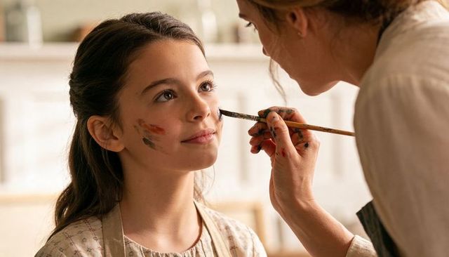 Mother painting daughter's cheek during at-home art session, face paint family bonding