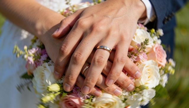 Close-up showing hands with gold wedding rings resting on bridal rose bouquet