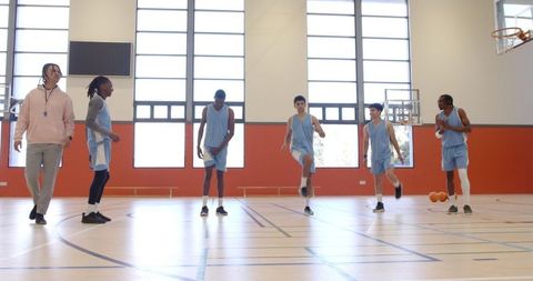Diverse basketball team warm-up with coach on indoor court