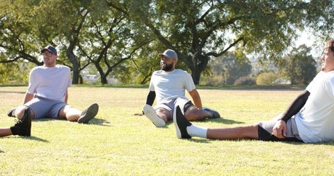 Diverse men stretching on park grass field preparing for team fitness and athletic training