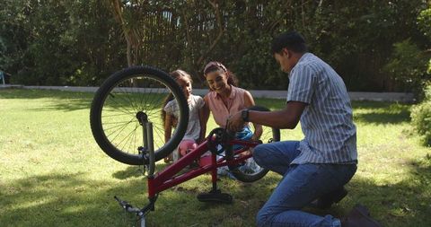 Family Repairing Bicycle Together Outdoors on Sunny Day