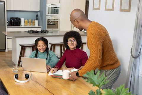Diverse family sharing coffee while working together at kitchen table with laptop