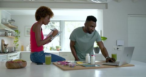 African american couple planning healthy meals and supplements in sunlit modern kitchen