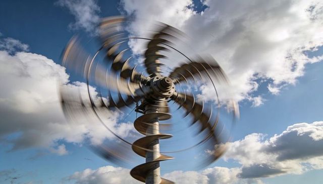 Spinning metallic kinetic sculpture with helical shaft rotating against blue sky