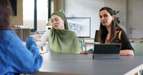 Multicultural female team meeting with woman in green hijab pointing at tablet