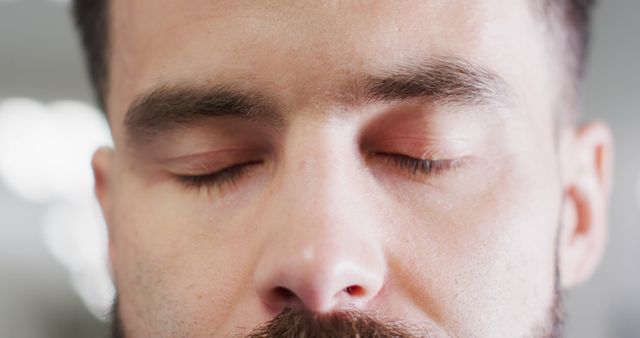 This close-up of a man with eyes closed depicts tranquility and peacefulness, making it ideal for content related to mindfulness, meditation, mental health, stress relief, and self-care. It can be used in wellness blogs, mental health articles, and advertisements for relaxation techniques or meditation apps.
