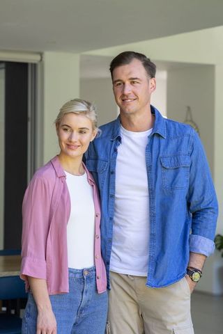 Young couple standing in modern open-plan home wearing casual denim and pastel shirts