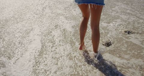 Woman's Legs Walking on Beach with Waves in Sunshine