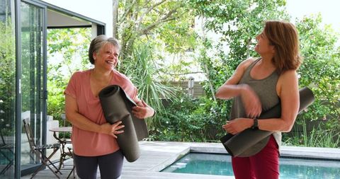Companionship and fitness: women holding yoga mats by pool