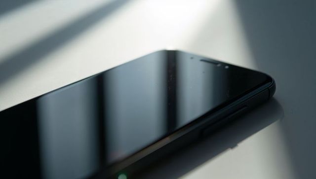 Sunlit black smartphone resting on table with smudged screen and diagonal blind shadows