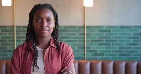 Confident african woman standing in cozy cafe with green tile wall and leather banquette