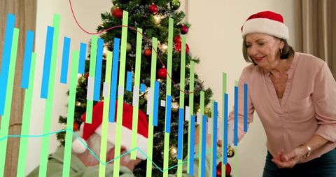 Senior woman placing ornament on decorated christmas tree with festive data overlay