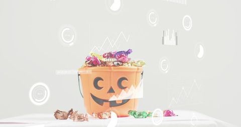 Halloween Jack-o'-Lantern Candy Bucket Brimming with Colorful Foil Sweets on White Tabletop