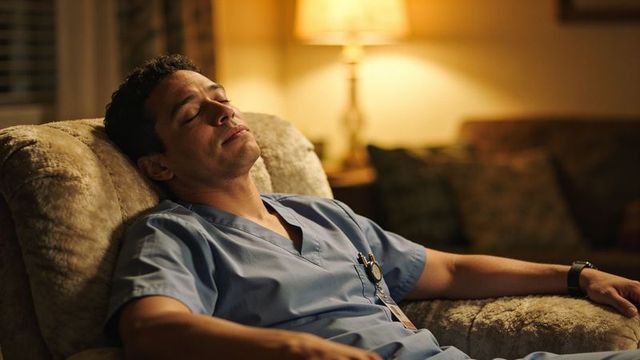 Night-shift medical worker resting in recliner after long shift with warm home lighting