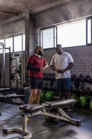 African american men chatting between sets in industrial gym with dumbbells and sunlight